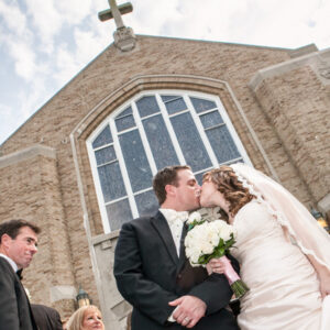 Bride and Groom Kissing in Front of Church Low angle pose of Bride and Groom Kissing in Front of Church showing Cross